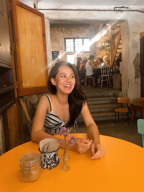 a woman smiles as she sits in a cafe full of plants