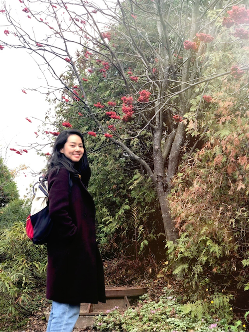 a woman smiles as she stands in front of a budding tree