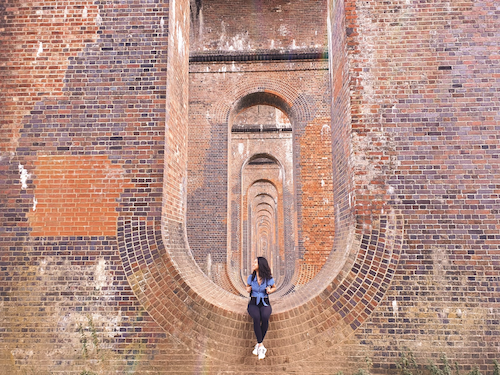 a woman sits below a brick viaduct